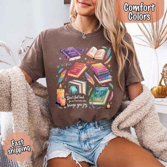 May include colorful illustrated books from the “A Court of Thorns and Roses” series surrounded by feathers, candles, and stars, with the quote “Don’t feel bad for one moment about what brings you joy,” celebrating fantasy fiction and book lover pride.