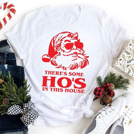 White t-shirt with red Santa Claus graphic and text, surrounded by Christmas decor.