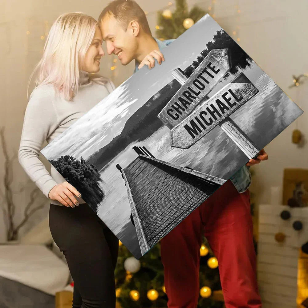 Smiling couple holding custom canvas print with names, lakeside dock, holiday background