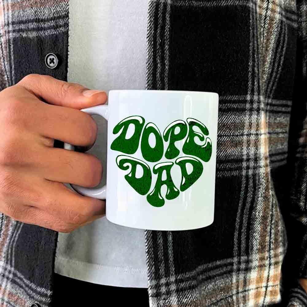 Person holding white mug with green 'Dope Dad' text, wearing plaid shirt