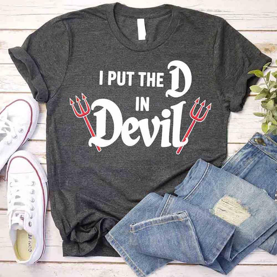 Gray t-shirt with 'I Put the D in Devil' text and designs, paired with jeans and sneakers on a wooden surface.