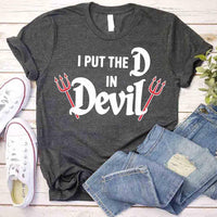 Gray t-shirt with 'I Put the D in Devil' text and designs, paired with jeans and sneakers on a wooden surface.