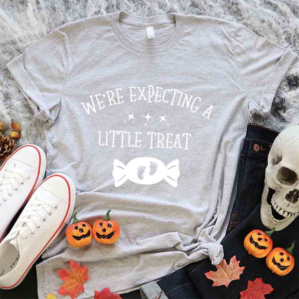 May include matching couple Halloween pregnancy announcement shirts, one reading ‘We’re Expecting a Little Treat’ with candy and baby footprints, and the other reading ‘It’s Not Trick’ with candy graphic – fun maternity reveal apparel.