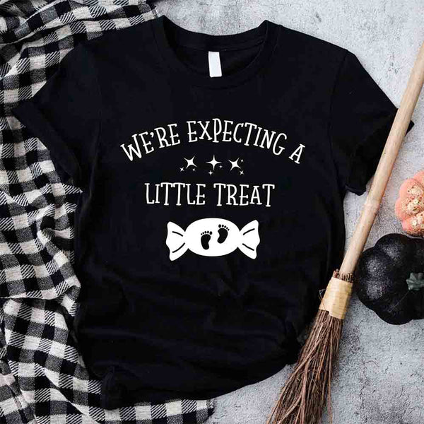 May include matching couple Halloween pregnancy announcement shirts, one reading ‘We’re Expecting a Little Treat’ with candy and baby footprints, and the other reading ‘It’s Not Trick’ with candy graphic – fun maternity reveal apparel.