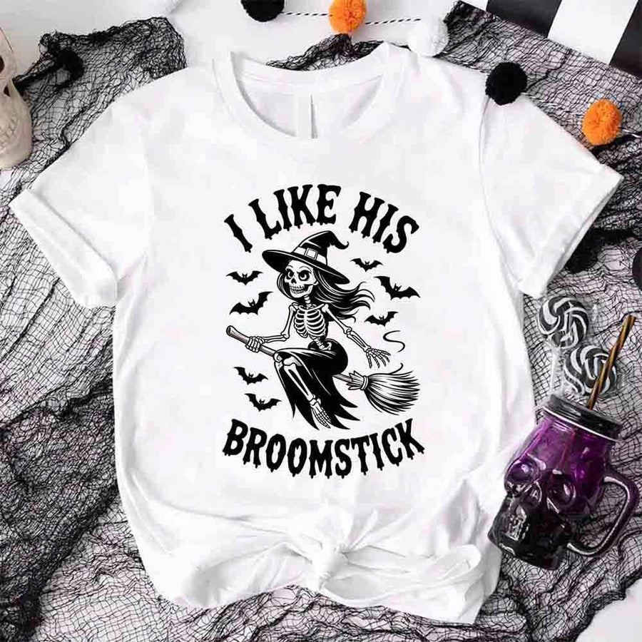 White t-shirt with skeleton design and text 'I Like His Broomstick' on a Halloween-themed background.
