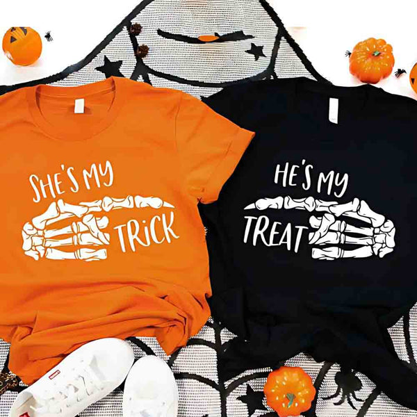 May include matching couple Halloween shirts with skeleton hand graphics, one reading ‘She’s My Trick’ on orange tee and the other reading ‘He’s My Treat’ on black tee – funny spooky couple apparel.
