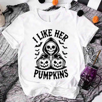 White t-shirt with Halloween-themed design featuring a skeleton holding pumpkins and text 'I Like Her Pumpkins' on a spider web background.