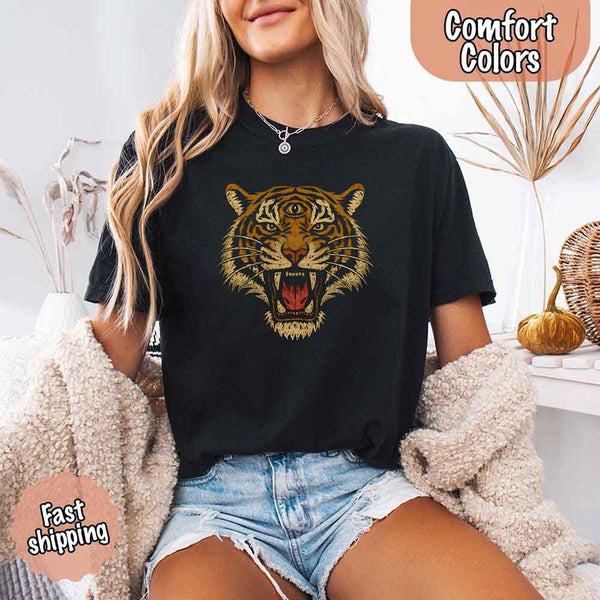 May include a woman wearing a black Comfort Colors T-shirt featuring a bold tiger graphic with 90s jungle safari vibes, styled casually with denim for a retro outdoor look.