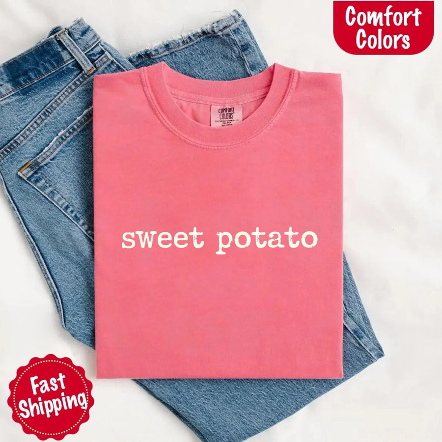 Pink t-shirt with 'sweet potato' text on a white background, folded next to blue jeans.