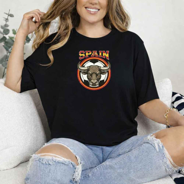 Woman wearing black Spain bull soccer fan t-shirt, sitting on a couch in ripped jeans.