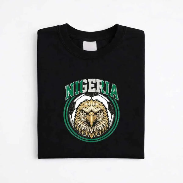 Black Nigeria soccer fan t-shirt with eagle and soccer ball graphic, folded on white background.
