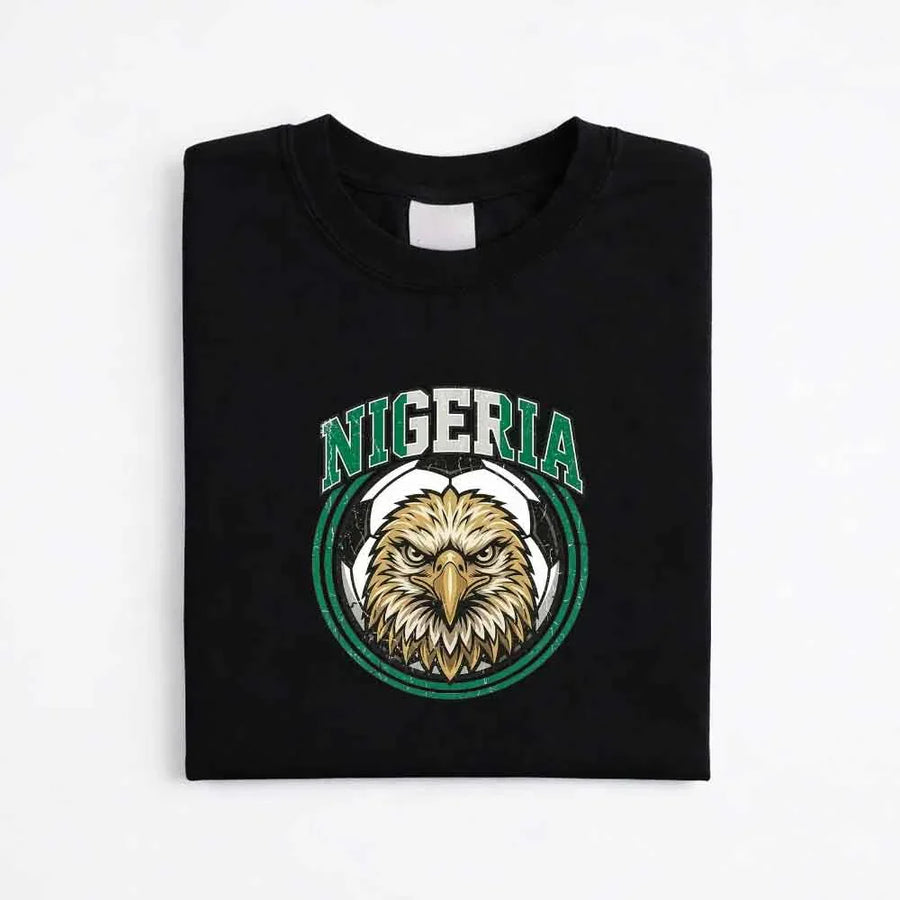 Black Nigeria soccer fan t-shirt with eagle and soccer ball graphic, folded on white background.