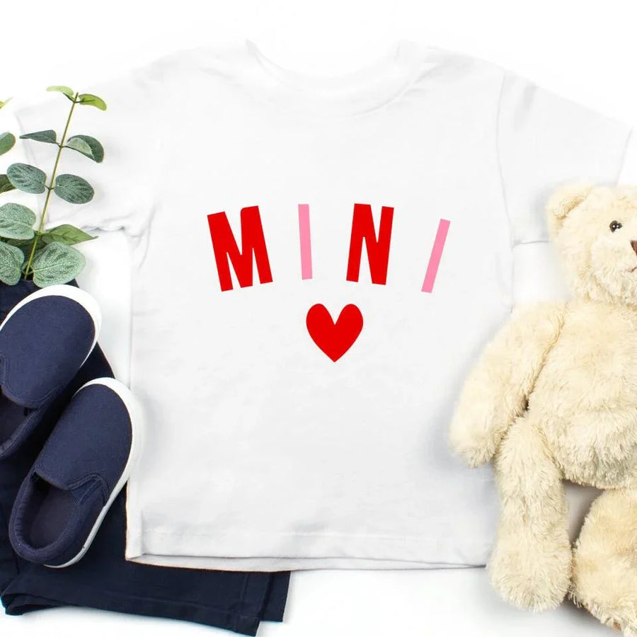 White shirt with red text and heart, navy shoes, and beige teddy bear on a white background