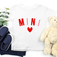 White shirt with red text and heart, navy shoes, and beige teddy bear on a white background