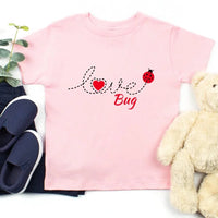 Pink t-shirt with 'love bug' design, navy shoes, and teddy bear on a white background