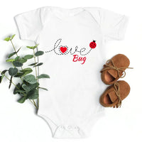 White baby onesie with 'Love Bug' text, green leaves, and brown baby shoes on a white background