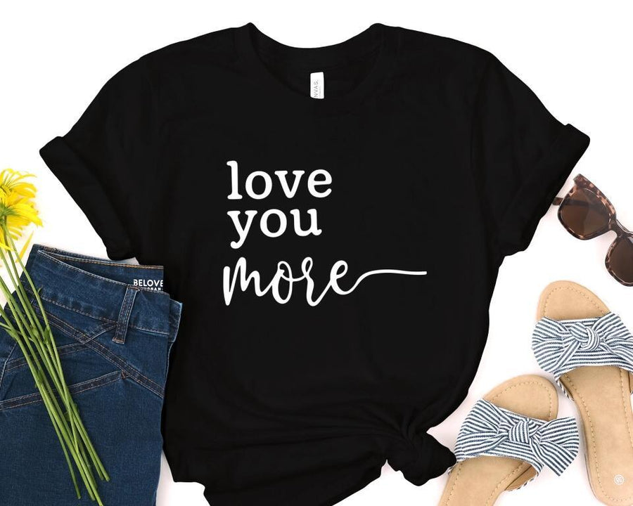 Black t-shirt with 'love you more' text, jeans, sandals, and sunglasses on a white background