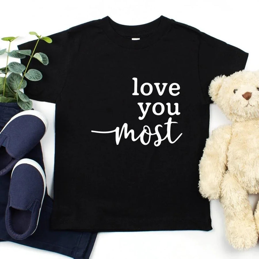 Black t-shirt with 'love you most' text, navy shoes, and a teddy bear on a white background