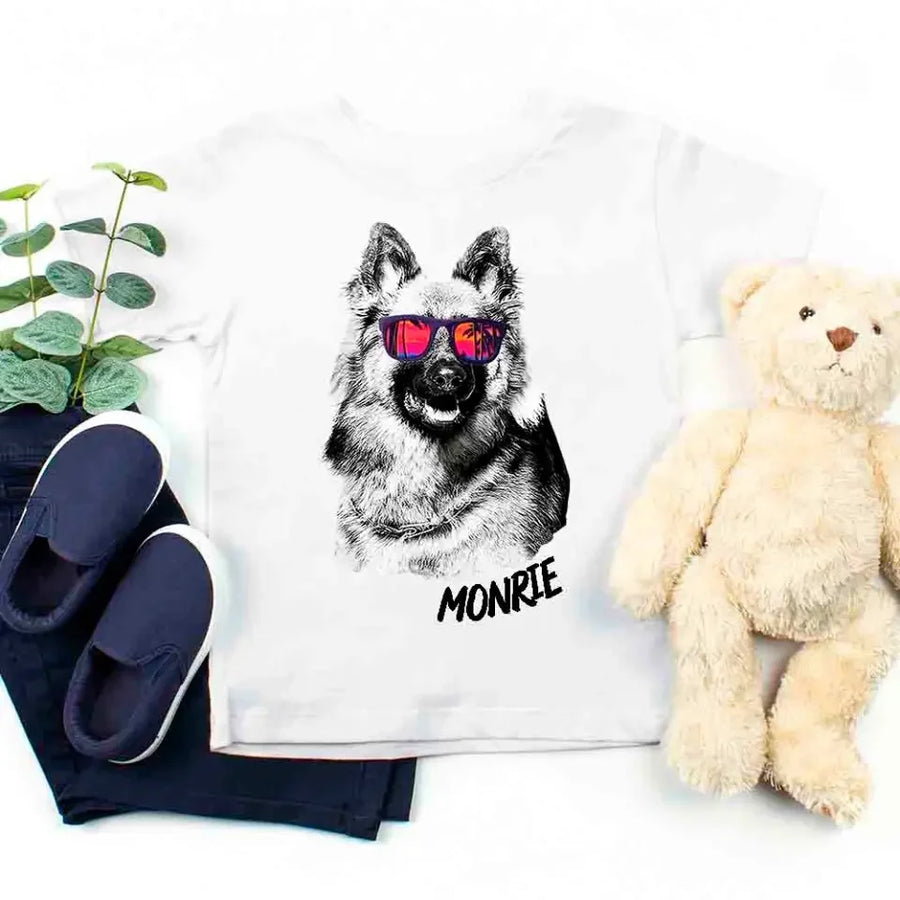 White pillow with a dog illustration and 'MONIE' text, surrounded by navy slippers, a plant, and a teddy bear on a white background.
