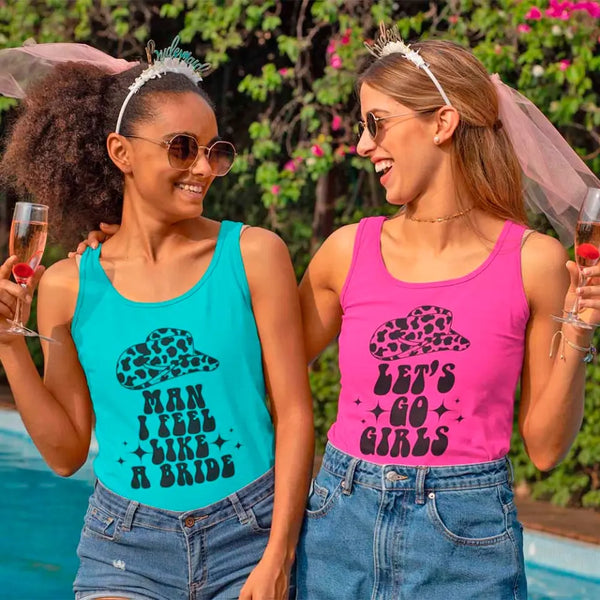 Two women in tank tops with bridal-themed decorations, holding glasses with a pool and trees in the background.