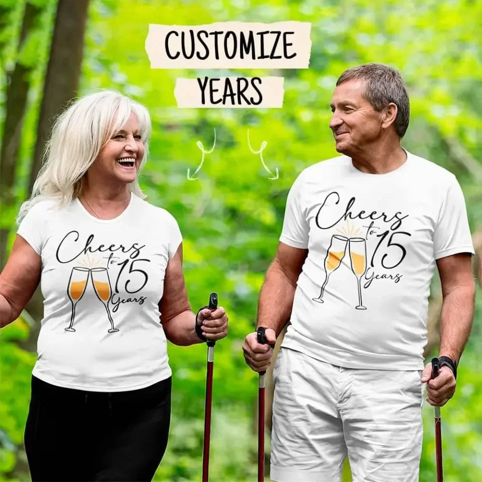Two people wearing white t-shirts with 'Cheers to 15 Years' text and champagne glass graphics, standing outdoors.