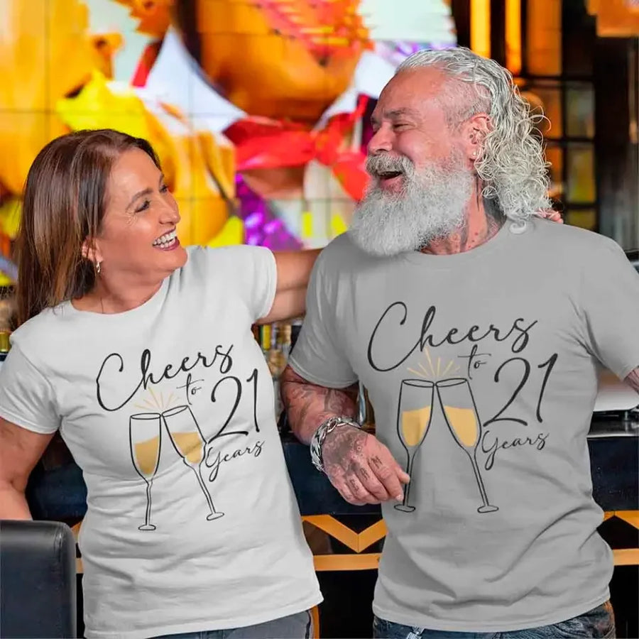 Two people wearing matching t-shirts with 'Cheers to 21 Years' design in a festive setting.