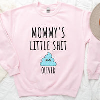 A white t-shirt with the text 'MOMMY'S LITTLE SHIT' printed on the front, above a cartoon graphic of a cloud with the name 'Oliver' added below the graphic.