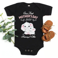 Black baby onesie with 'Our First Mother's Day 2025 Mommy & Ollie' text and elephant graphics, placed on a white background with shoes and plant.