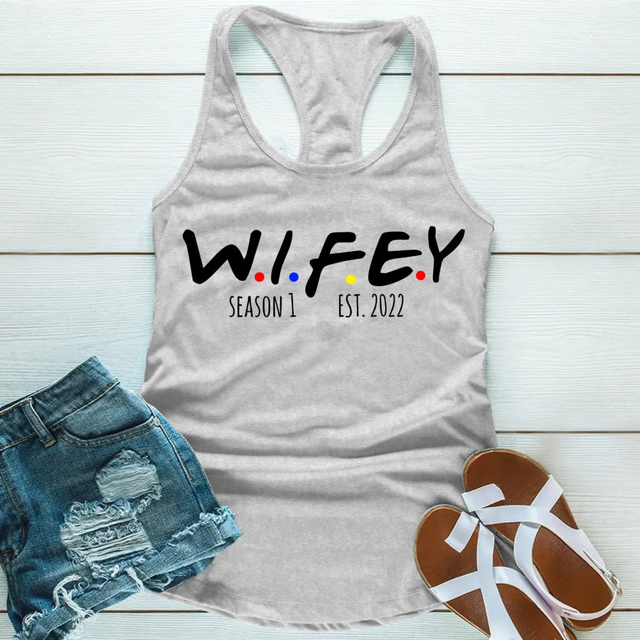 Gray tank top with 'WIFEY' text, denim shorts, and sandals on a light wooden surface
