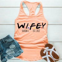 Peach tank top with 'WIFEY' text, denim shorts, and sandals on a wooden surface