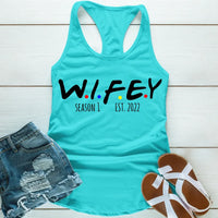 Turquoise tank top with 'WIFEY' text, denim shorts, and sandals on a wooden surface