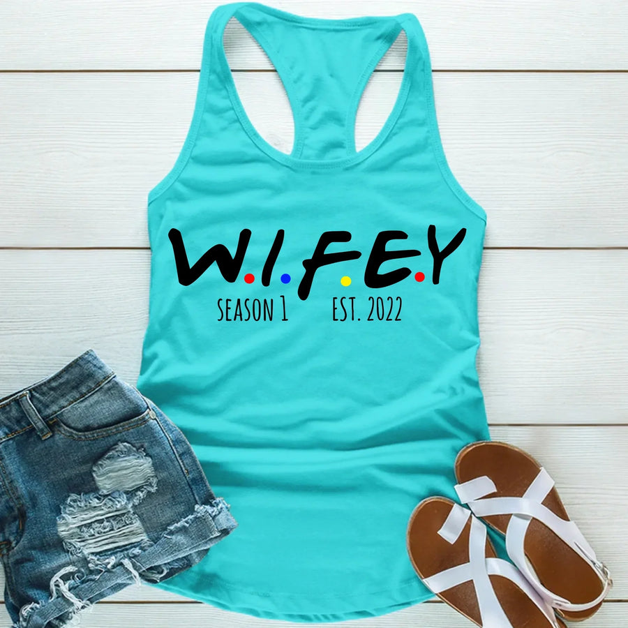Turquoise tank top with 'WIFEY' text, denim shorts, and sandals on a wooden surface