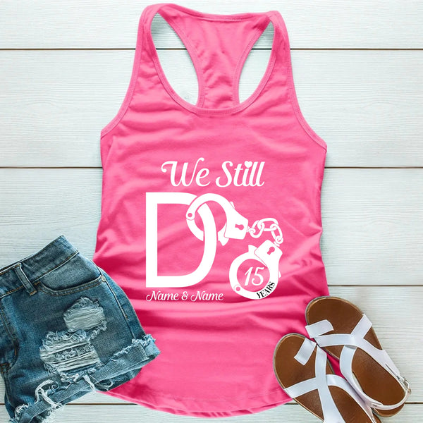 Pink tank top with 'We Still Do' design, denim shorts, and sandals on a wooden surface