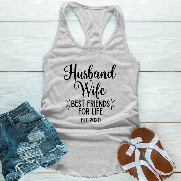 Gray tank top with 'Husband Wife Best Friends for Life Est. 2020' text, paired with denim shorts and sandals on a light wooden surface.