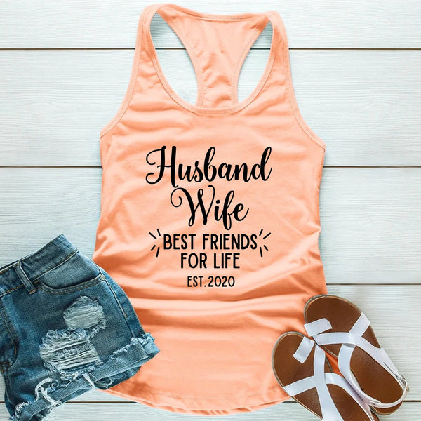 Peach tank top with 'Husband Wife Best Friends for Life Est. 2020' text, denim shorts, and sandals on a light wooden surface.