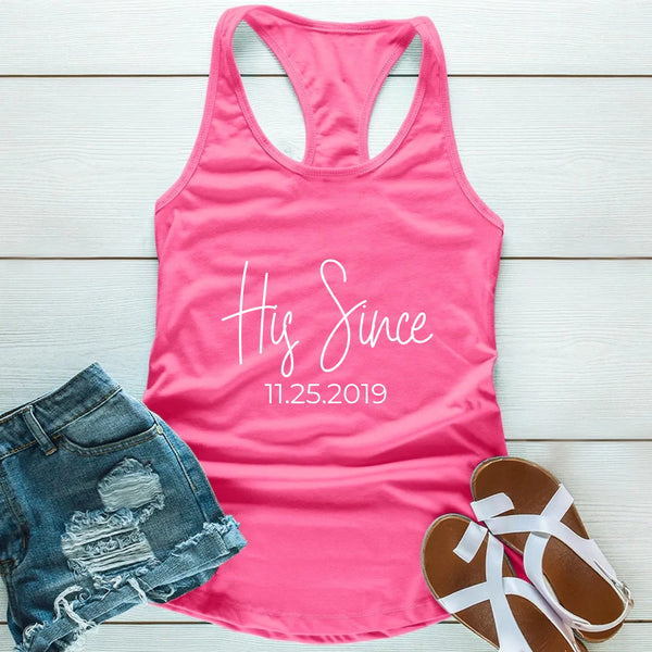 Pink tank top with 'His Since 11.25.2019' text, denim shorts, and sandals on a wooden surface.