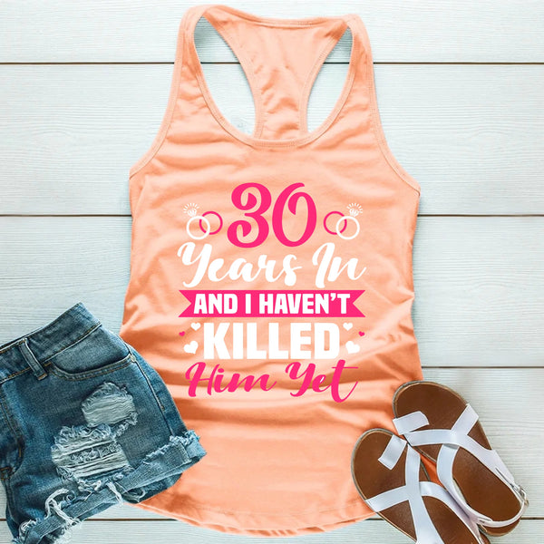 Peach tank top with humorous text, denim shorts, and sandals on a light wooden surface