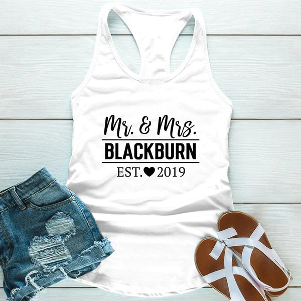 White tank top with 'Mr & Mrs. Blackburn EST. 2019' text, paired with denim shorts and sandals on a light wooden surface.