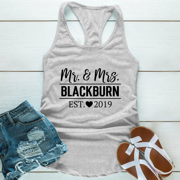 Gray tank top with 'Mr. & Mrs. Blackburn EST. 2019' text, paired with denim shorts and sandals on a light wooden surface.