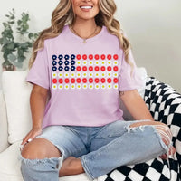 Woman wearing a lavender t-shirt with a floral American flag design, sitting on a couch