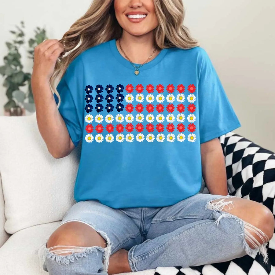 Woman wearing blue t-shirt with floral American flag design, sitting on couch in ripped jeans
