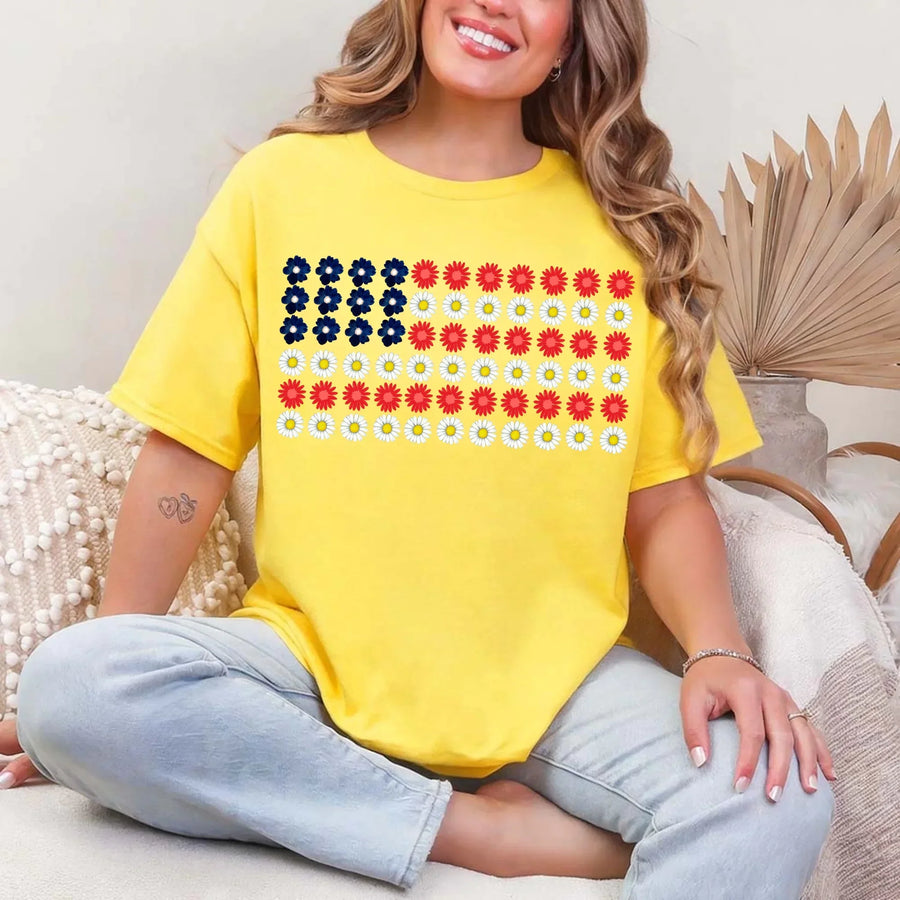 Woman wearing a yellow t-shirt with an American flag floral print design, sitting indoors.