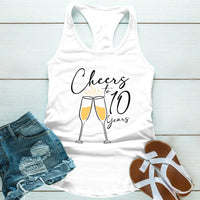 White tank top with 'Cheers to 10 Years' text and champagne glass design, paired with denim shorts and sandals on a light wooden surface.