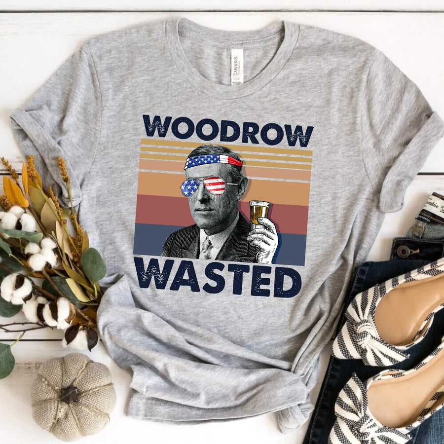 Gray t-shirt with a graphic of Woodrow Wilson and 'WOODROW WASTED' text, placed on a surface with decorative items.