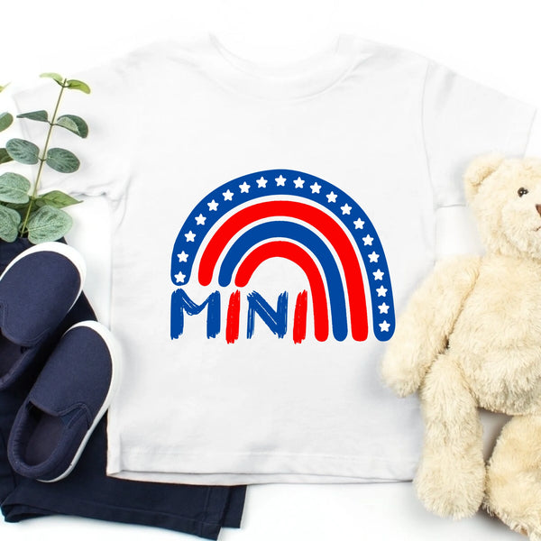 White shirt with rainbow and 'MINI' design, navy shoes, and beige teddy bear on a white background