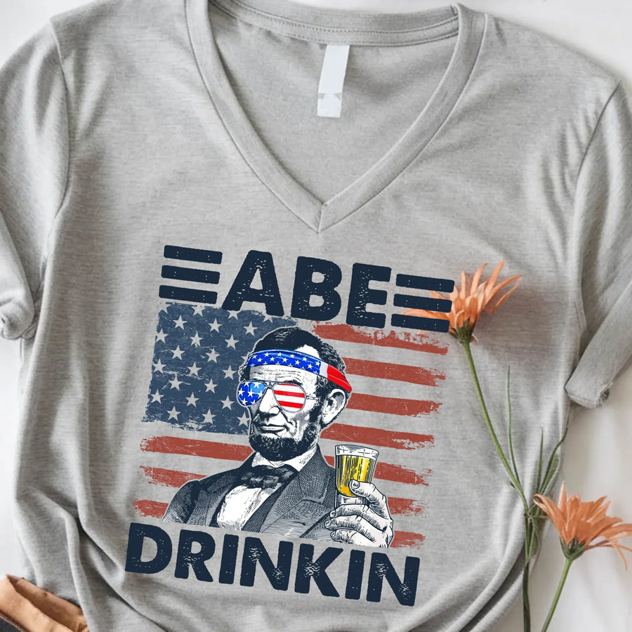 Grey patriotic tee with Abe Lincoln in USA sunglasses, beer, and American flag graphic