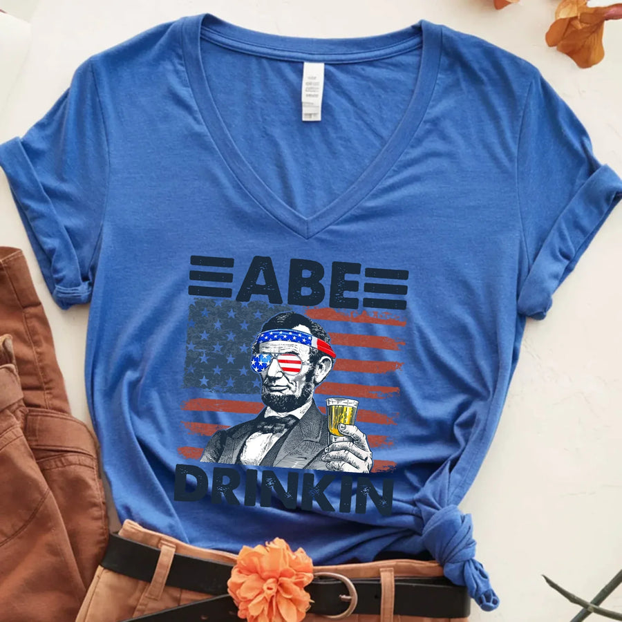 Blue v-neck tee with Abraham Lincoln holding a drink, American flag background, patriotic humor