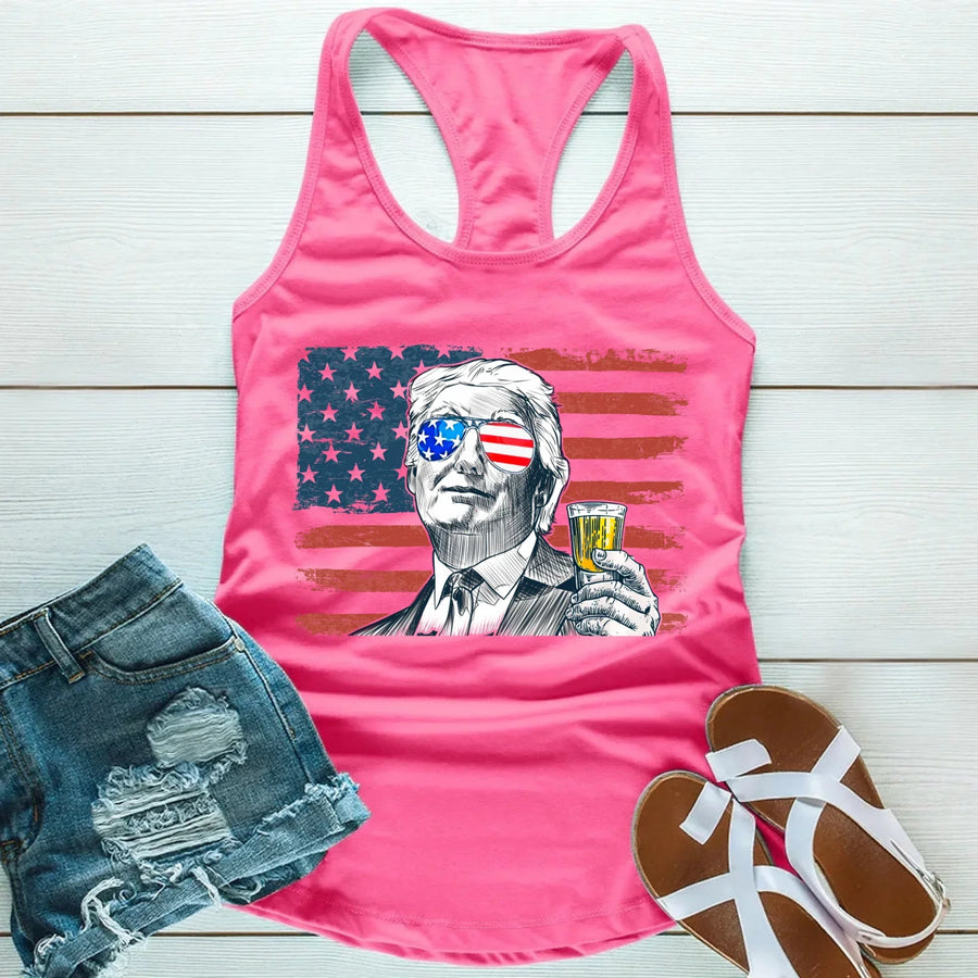 Pink tank top with graphic design of a person holding a drink, American flag, and denim shorts on a wooden surface.