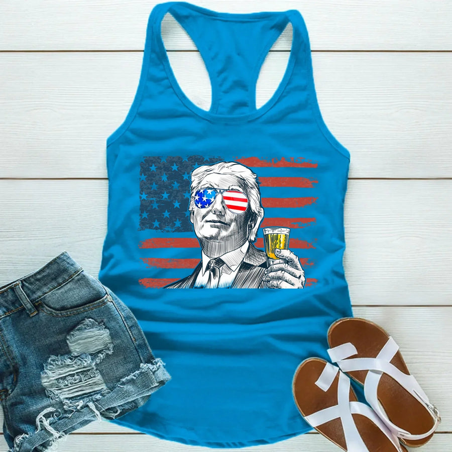 Blue tank top with graphic design of a person holding a drink, sunglasses with American flag pattern, and denim shorts and sandals on a wooden surface.