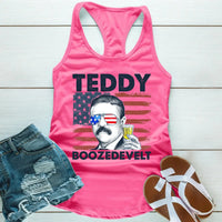 Pink tank top with a graphic of Teddy Roosevelt and text, paired with denim shorts and sandals on a wooden surface.